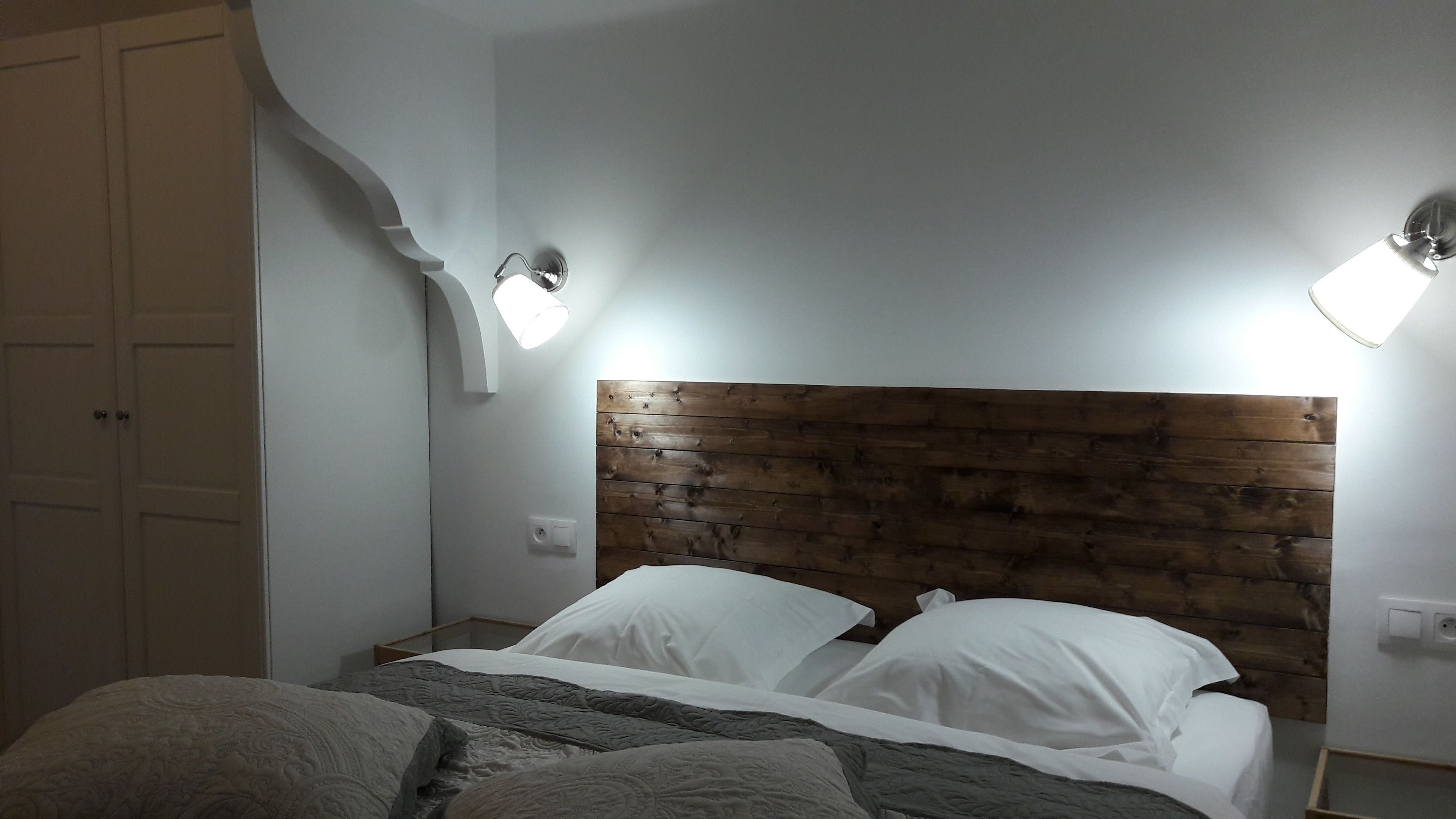 A bedroom with a wooden headboard, two bedside lamps, a bed with white bedding, and a white wardrobe with a curved design.