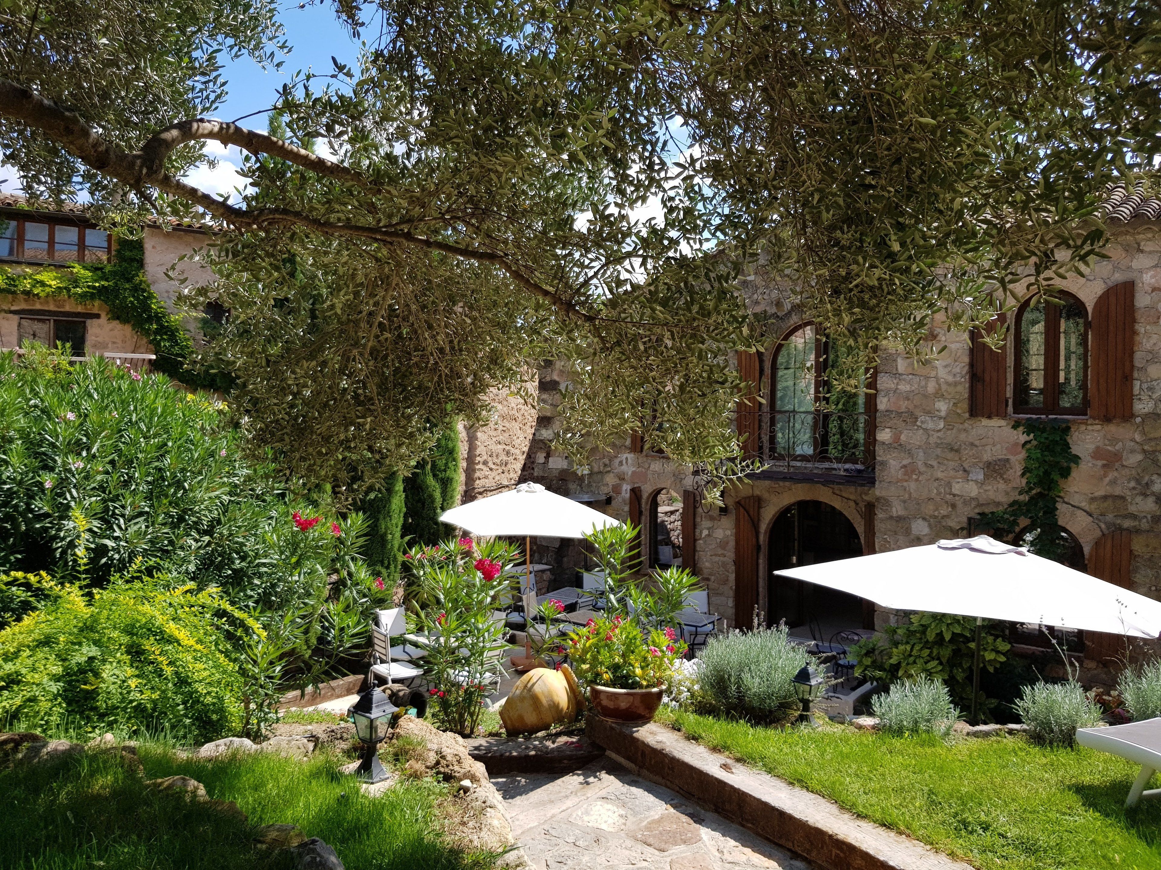 A courtyard with stone walls, potted plants, and outdoor seating under umbrellas.