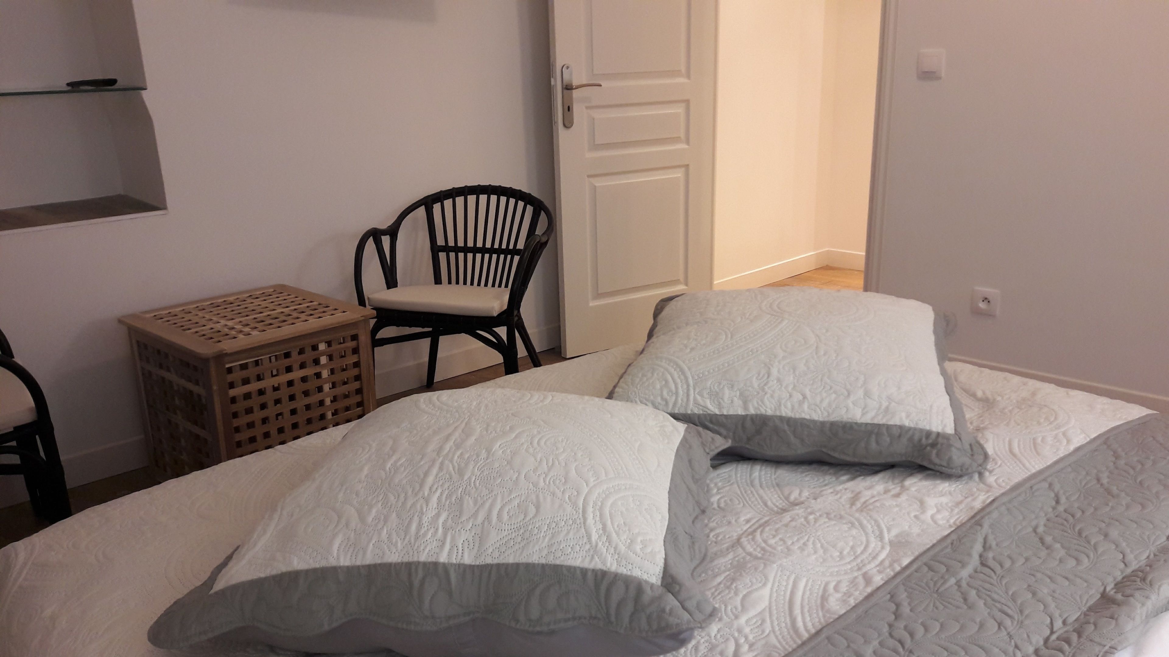Un dormitorio con cama, almohadas, una silla y una pequeña mesa de madera.