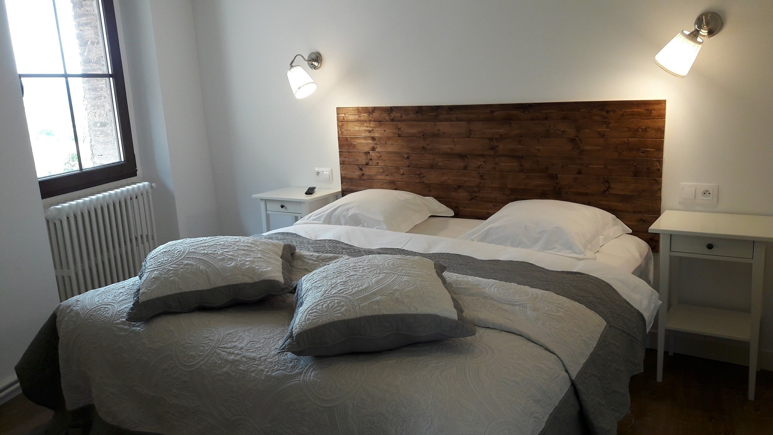 A neatly made bed with a wooden headboard, two bedside tables, and a window with a view.