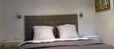 Un dormitorio con cabecera de madera, dos almohadas blancas, una colcha gris y un cuadro en la pared.
