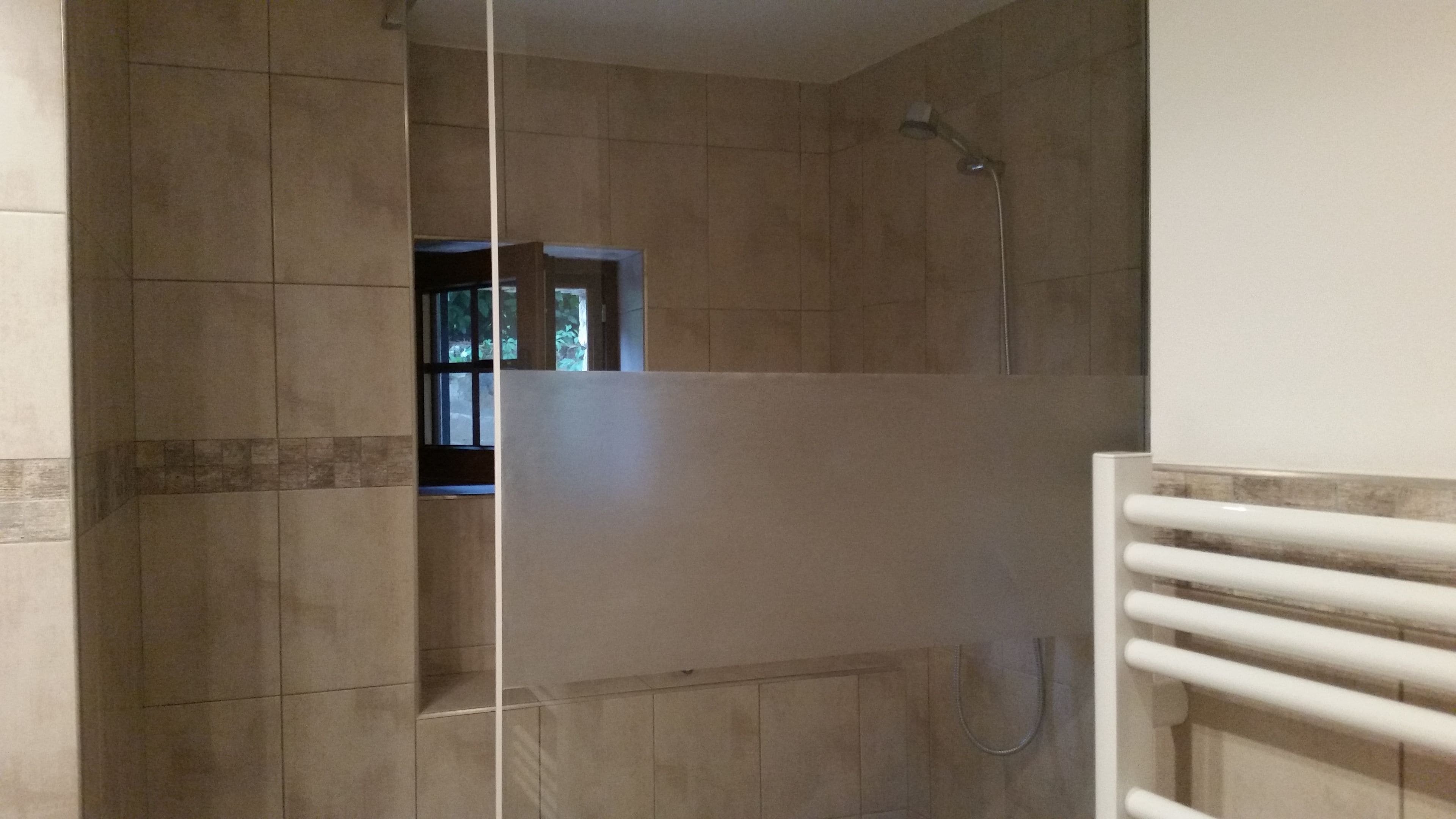 A bathroom with tiled walls, a shower area, and a window.