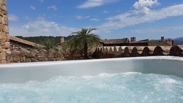 Un jacuzzi con un muro de piedra de fondo, una palmera y un edificio tradicional con techos de teja.