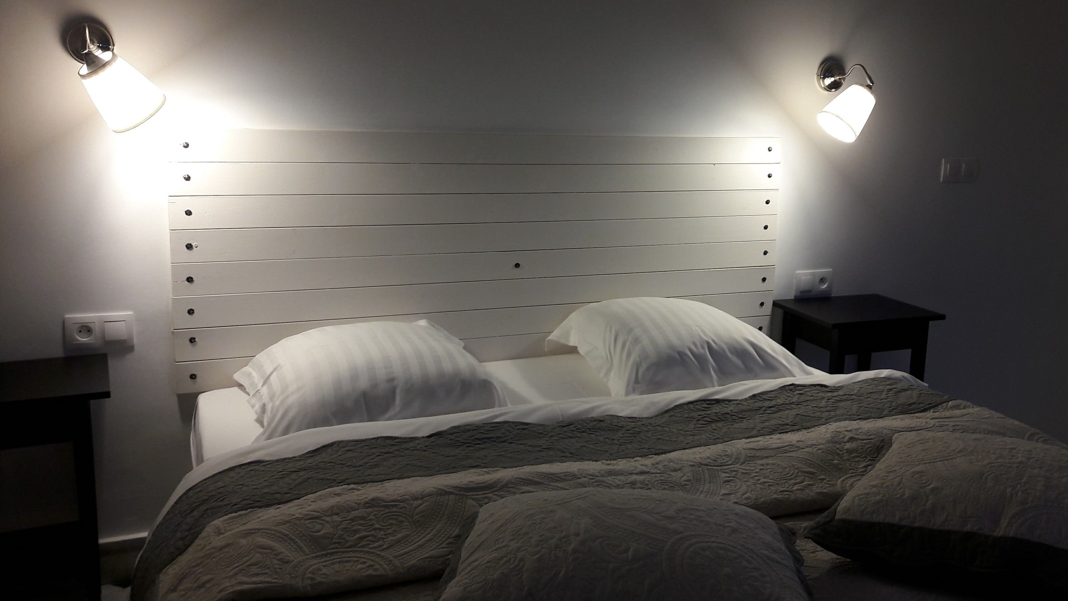 A bed with a wooden headboard, two bedside lamps, and a small nightstand.