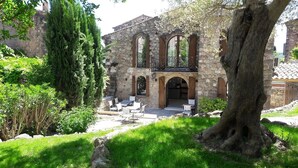Un edificio de piedra con patio, asientos exteriores y un gran árbol.