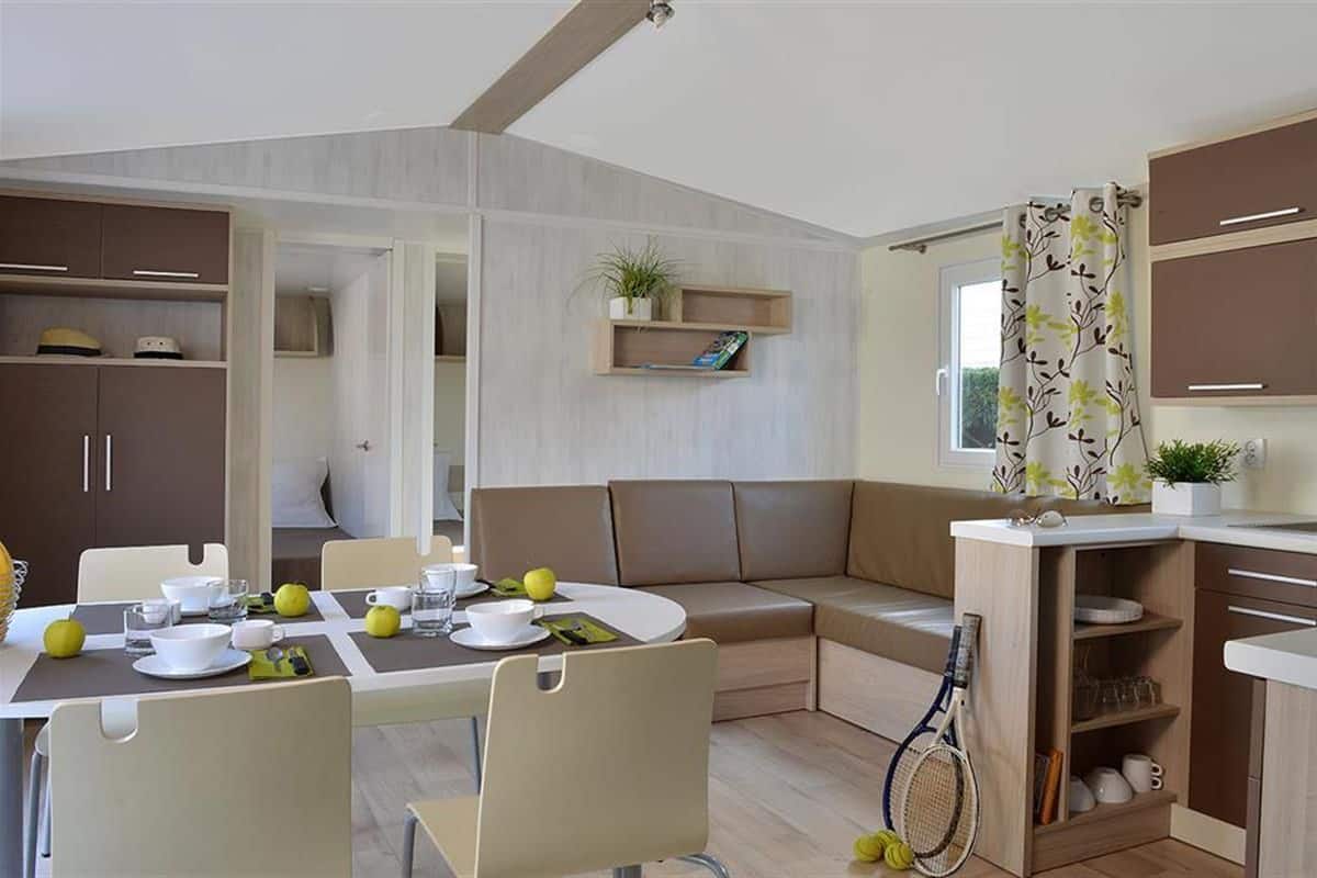 A compact living space with a dining area, a sofa, a small kitchen, and a window with curtains.