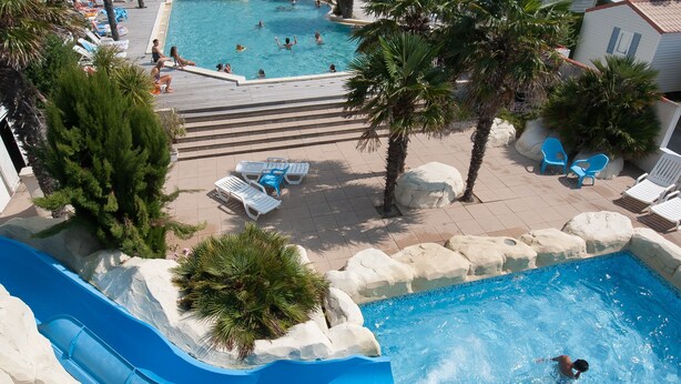Un resort con varias piscinas, palmeras y sillones de descanso.