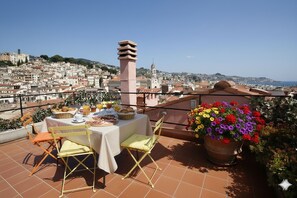 A terrace with a table set for breakfast, overlooking a cityscape with buildings and a tower. - Appartamento Manola (Sanremo)