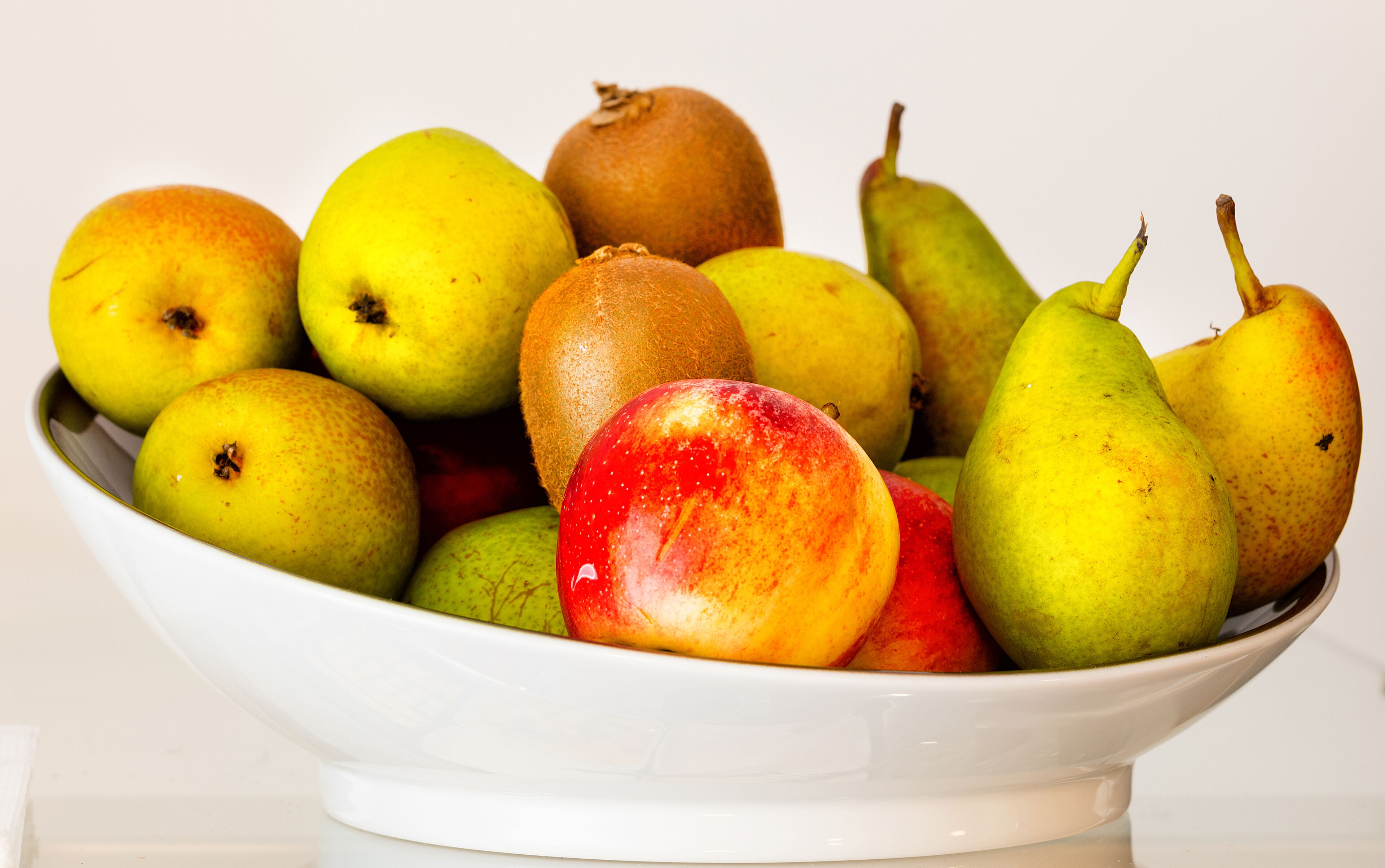 A white bowl filled with various fruits including pears, apples, and a kiwi.