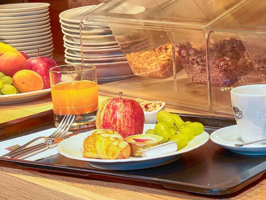 A breakfast tray with fruits, a glass of orange juice, a croissant, and a coffee cup.