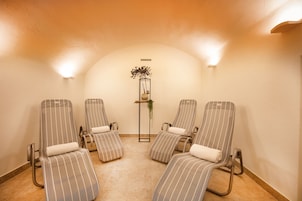 Un cuarto de spa con cuatro sillones reclinables a rayas, una planta pequeña sobre un pedestal y un suelo de baldosas.