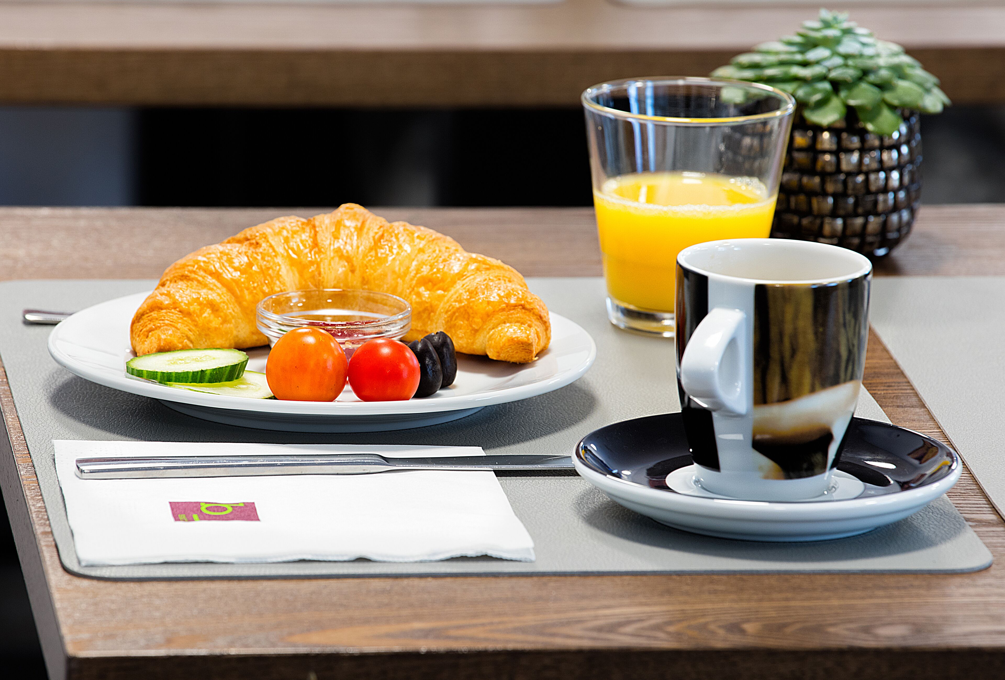 A breakfast setting with a croissant, fruit, a glass of orange juice, and a cup of coffee on a table.