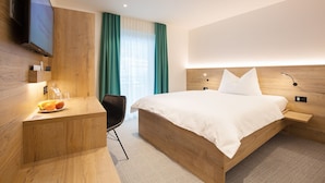 Una habitación de hotel moderna con una cama de madera, un escritorio con silla, un televisor de pantalla plana y un ventanal con cortinas.