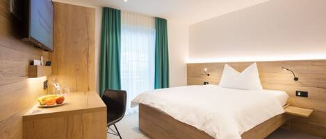 Una habitación de hotel moderna con una cama de madera, un escritorio con silla, un televisor de pantalla plana y un ventanal con cortinas.