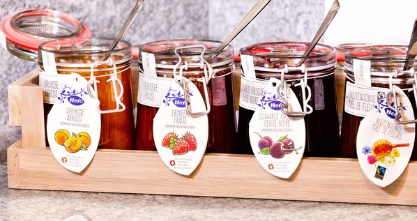 A wooden tray holding four glass jars of fruit preserves, each with a label indicating the type of preserve.