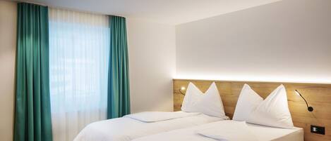 Habitación de hotel con una cama doble, cabecera de madera, mesita de noche y un ventanal con cortinas.