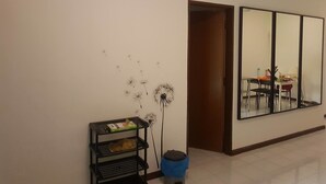 A hallway with a wall-mounted shelf holding a laptop and a trash bin. A large mirror reflects a dining area with chairs and a table. - Araaz Homestay (Seremban)