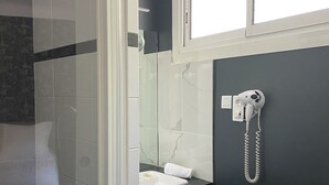 A bathroom with a glass shower door, a white sink, a towel rack, and a telephone. - Hotel Regina (Sète)
