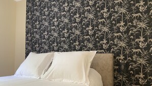 A neatly made bed with white linens in a room with a dark floral wallpaper. - Hotel Regina (Sète)