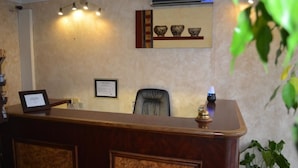 A reception desk with a framed certificate, a chair, and a wall-mounted air conditioner. - Hotel Regina (Sète)