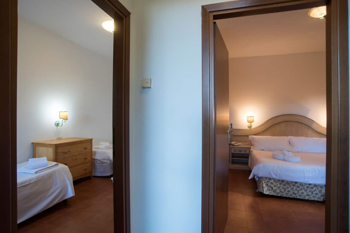 A hotel room with a bed, bedside table, lamp, and a wooden dresser.