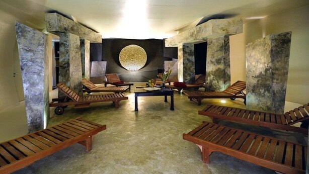 Un espace de détente avec des chaises longues en bois, une table centrale et un grand élément décoratif mural circulaire.