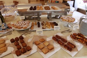 A buffet with various pastries and baked goods, including croissants, muffins, and donuts, arranged on plates and in baskets. - Antico Colle Toscano Resort (Arcidosso)