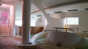 Un intérieur moderne avec une baignoire aux lignes courbes, un escalier et une fenêtre laissant entrer la lumière naturelle.