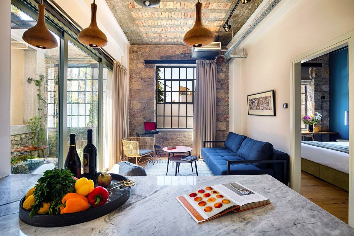 Uma sala de estar moderna com um sofá azul, uma mesa de mármore com uma cesta de frutas e um livro.