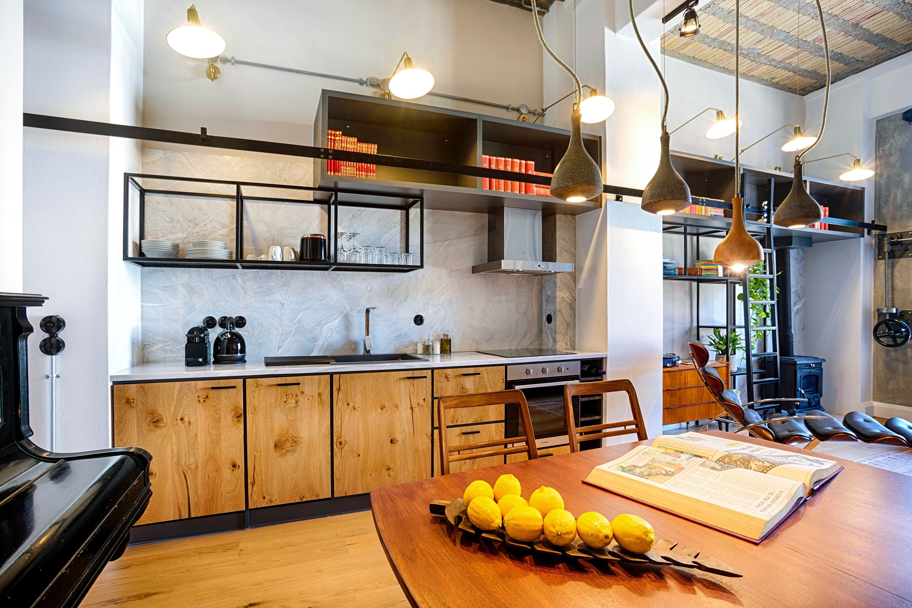 A modern kitchen with wooden cabinets, a dining table with lemons, and pendant lighting.