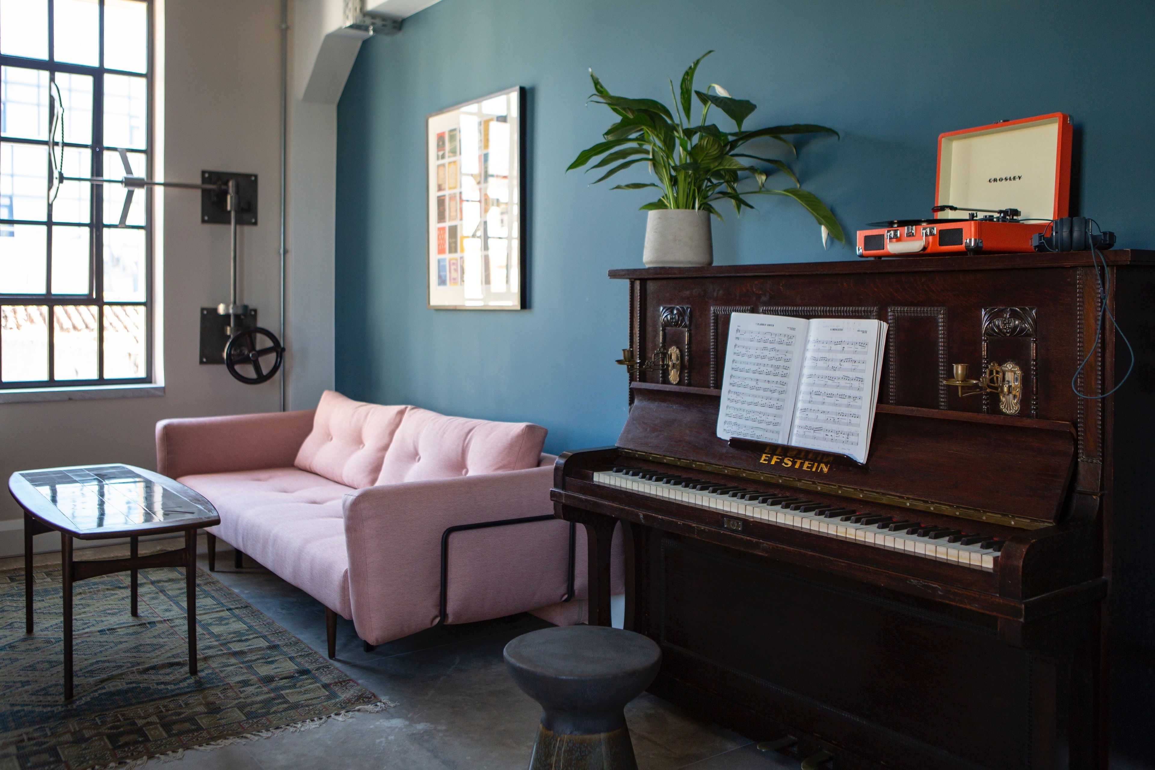A room with a piano, a pink sofa, a glass table, and a potted plant.