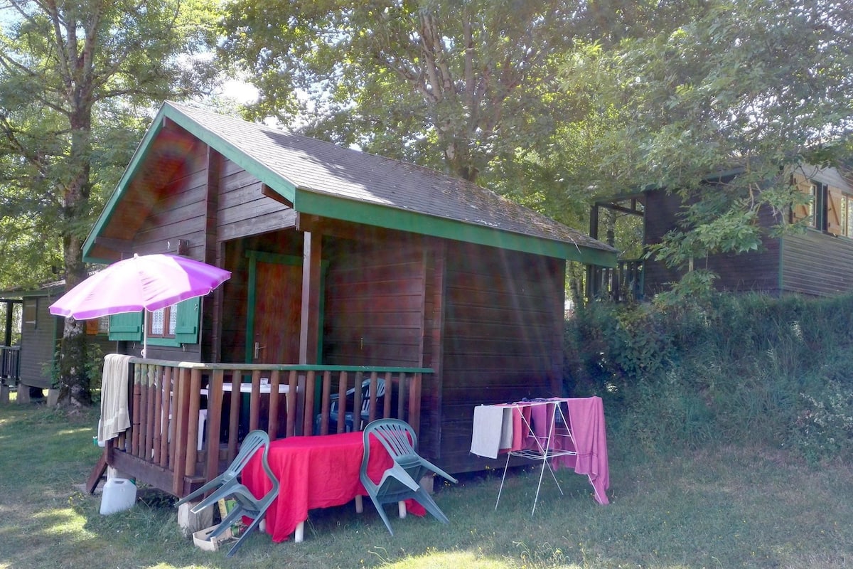 Een houten hut met een veranda, een tafel met een rode tafelkleed en een paarse parasol.