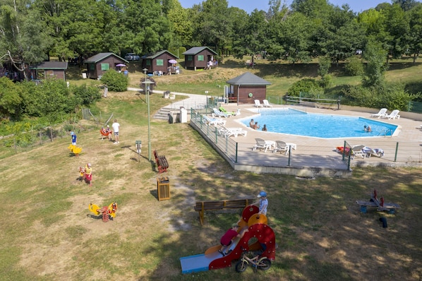 A swimming pool surrounded by a fenced area with lounge chairs and a playground. - Camping de Tauves (Tauves)