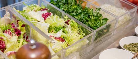 Una barra de ensaladas con diversas verduras frescas y hojas verdes.