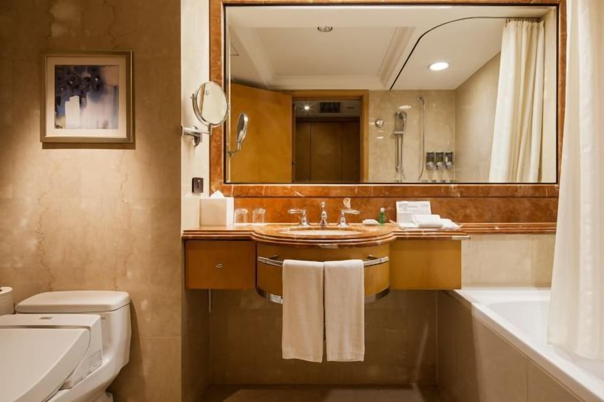 A modern bathroom with a marble vanity, a large mirror, a shower, and a toilet.