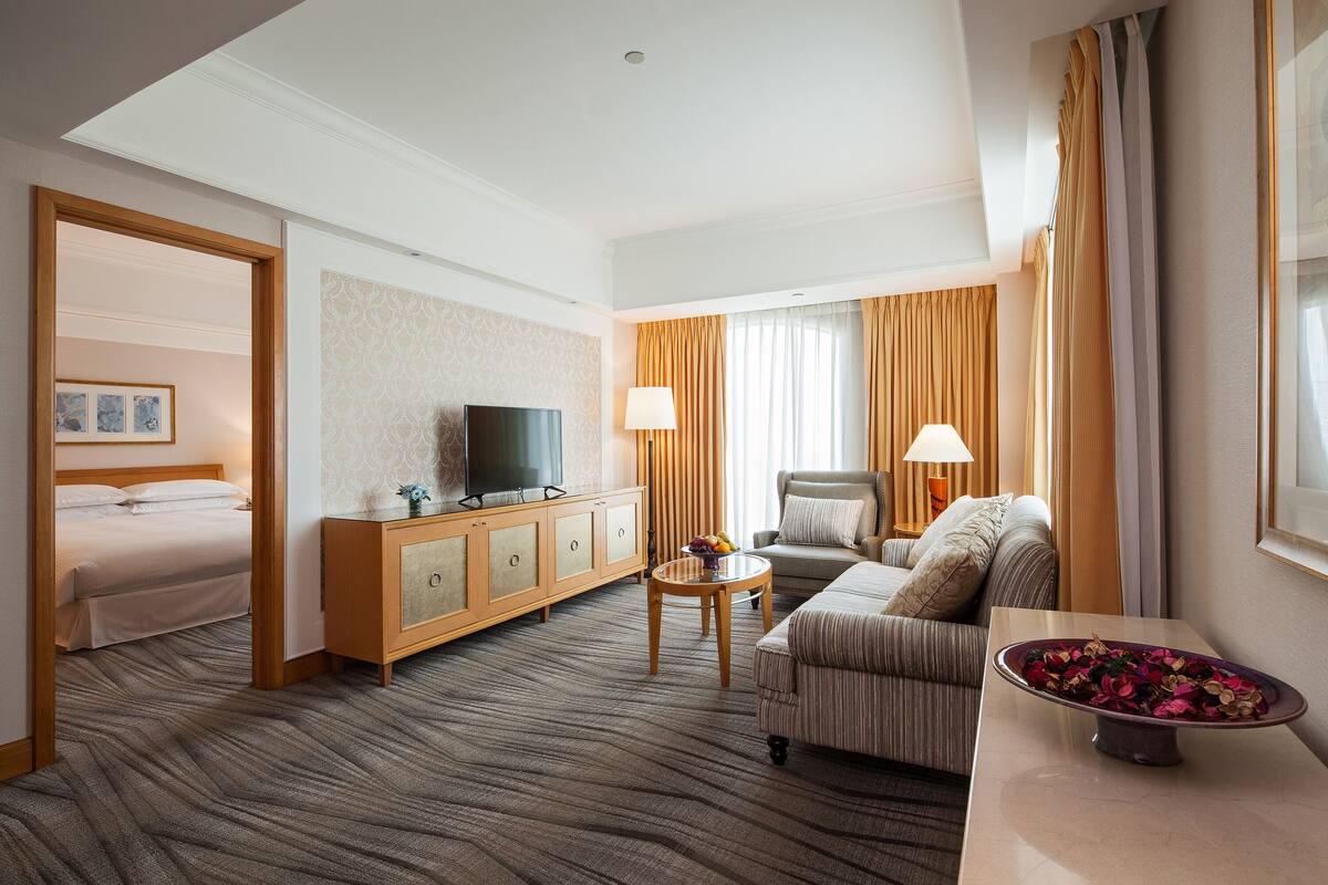 Hotellihuone, jossa on sänky, televisio, sohva, sohvapöytä ja koristeellinen kulho.