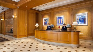 Een receptiebalie met twee receptionisten, lijstwerk aan de muur en een vloer met patroon.