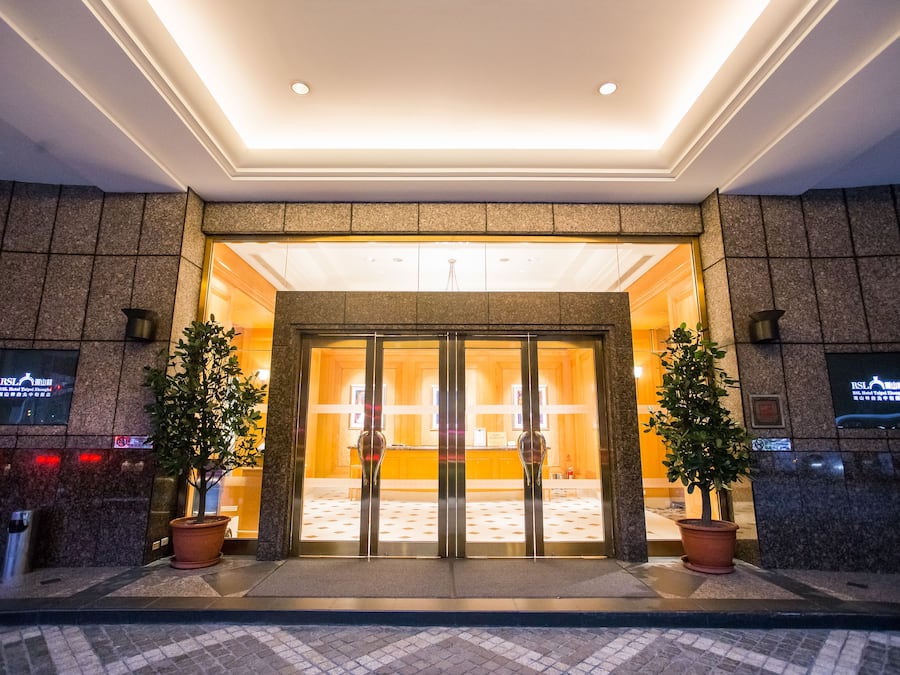 A hotel entrance with a glass door, potted plants, and a tiled floor.