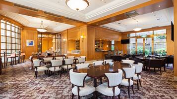 A spacious conference room with a large wooden table surrounded by chairs, a bar area with shelves of bottles, and large windows providing natural light.