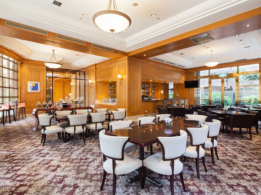 A spacious conference room with a large wooden table surrounded by chairs, a bar area with shelves of bottles, and large windows providing natural light.