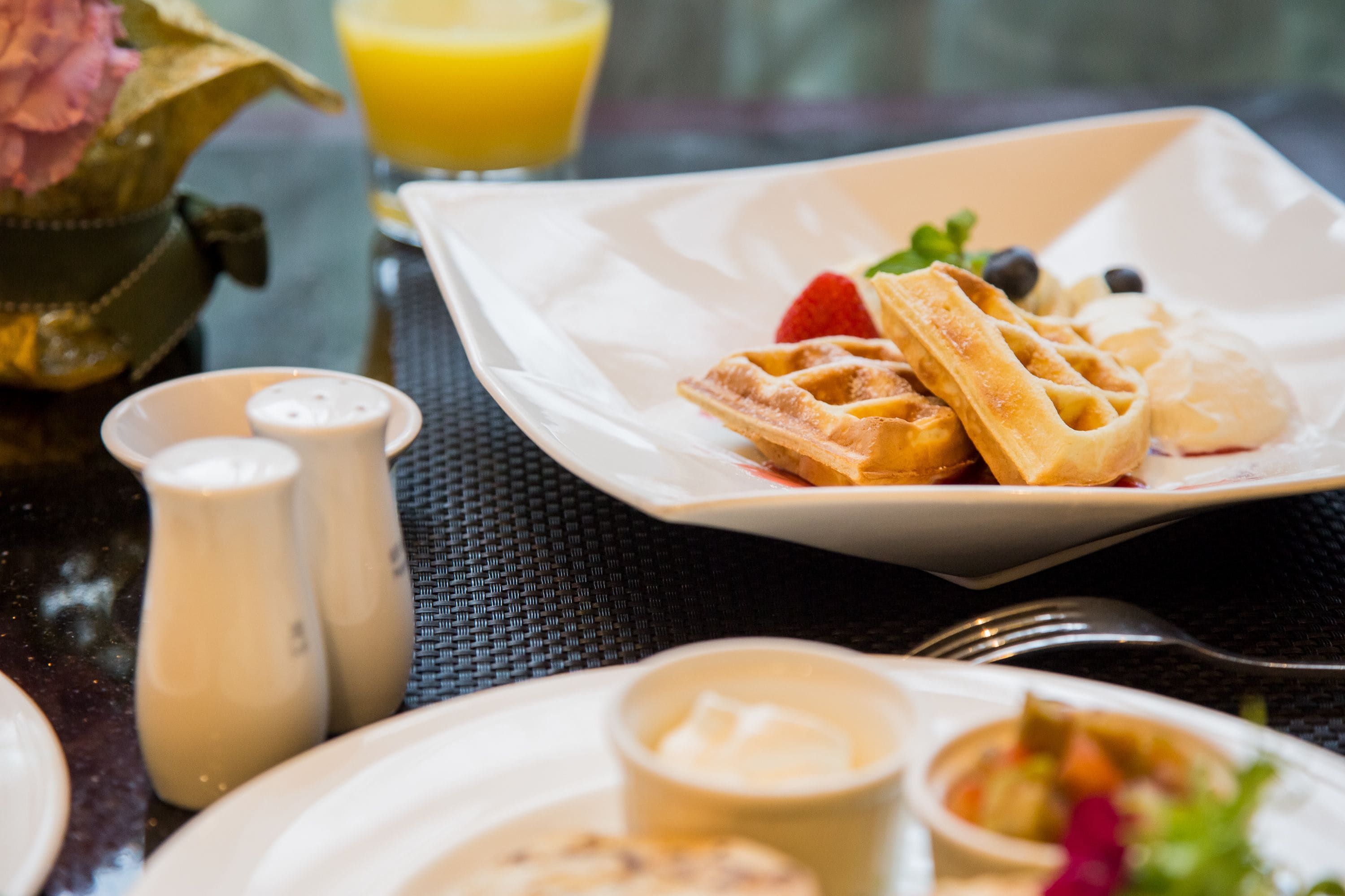 A breakfast setting with waffles, berries, and a glass of orange juice on a table.