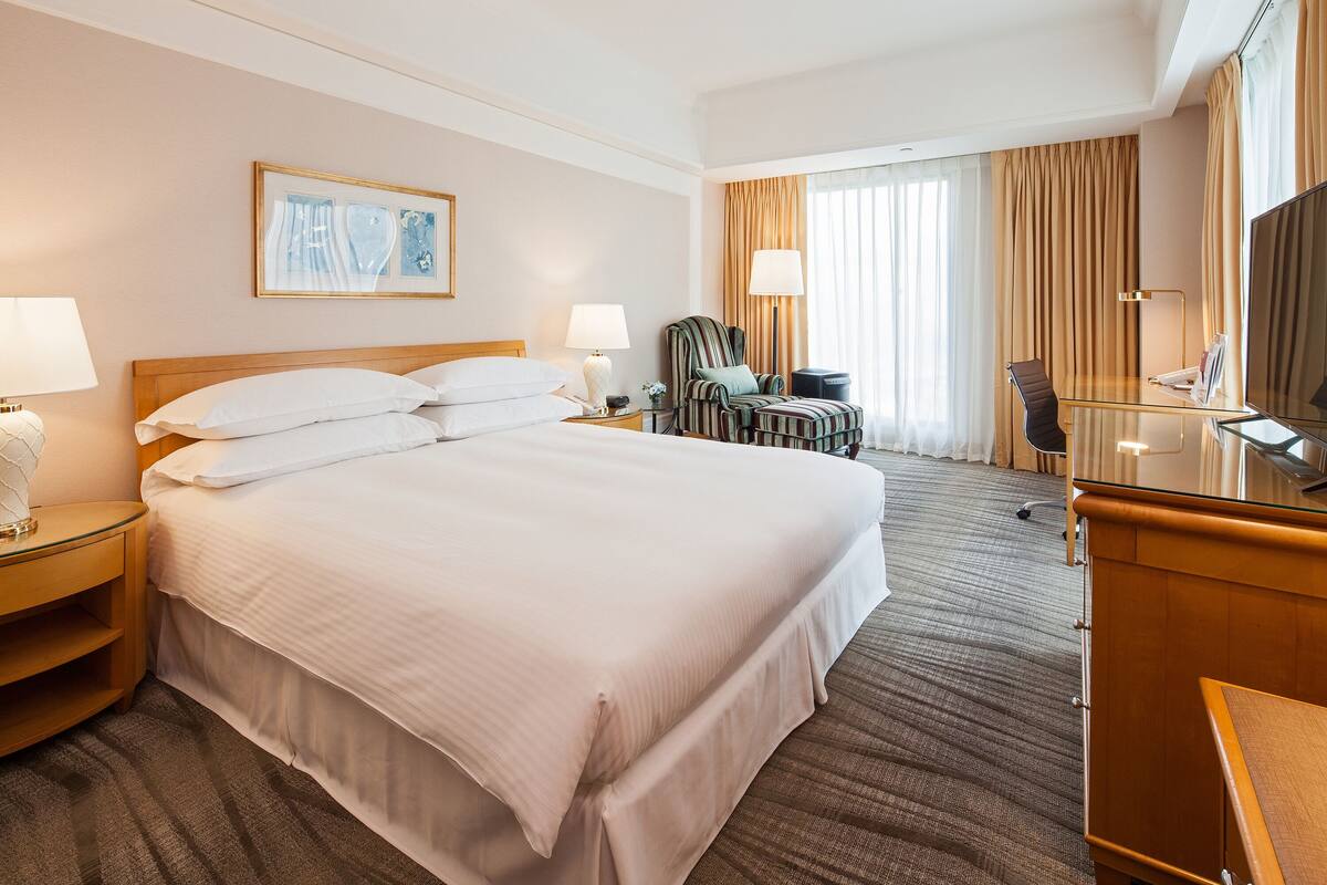 Hotellihuone, jossa on suuri sänky, kaksi yöpöytää, tuoli, työpöytä, televisio ja ikkuna, jossa on verhot.