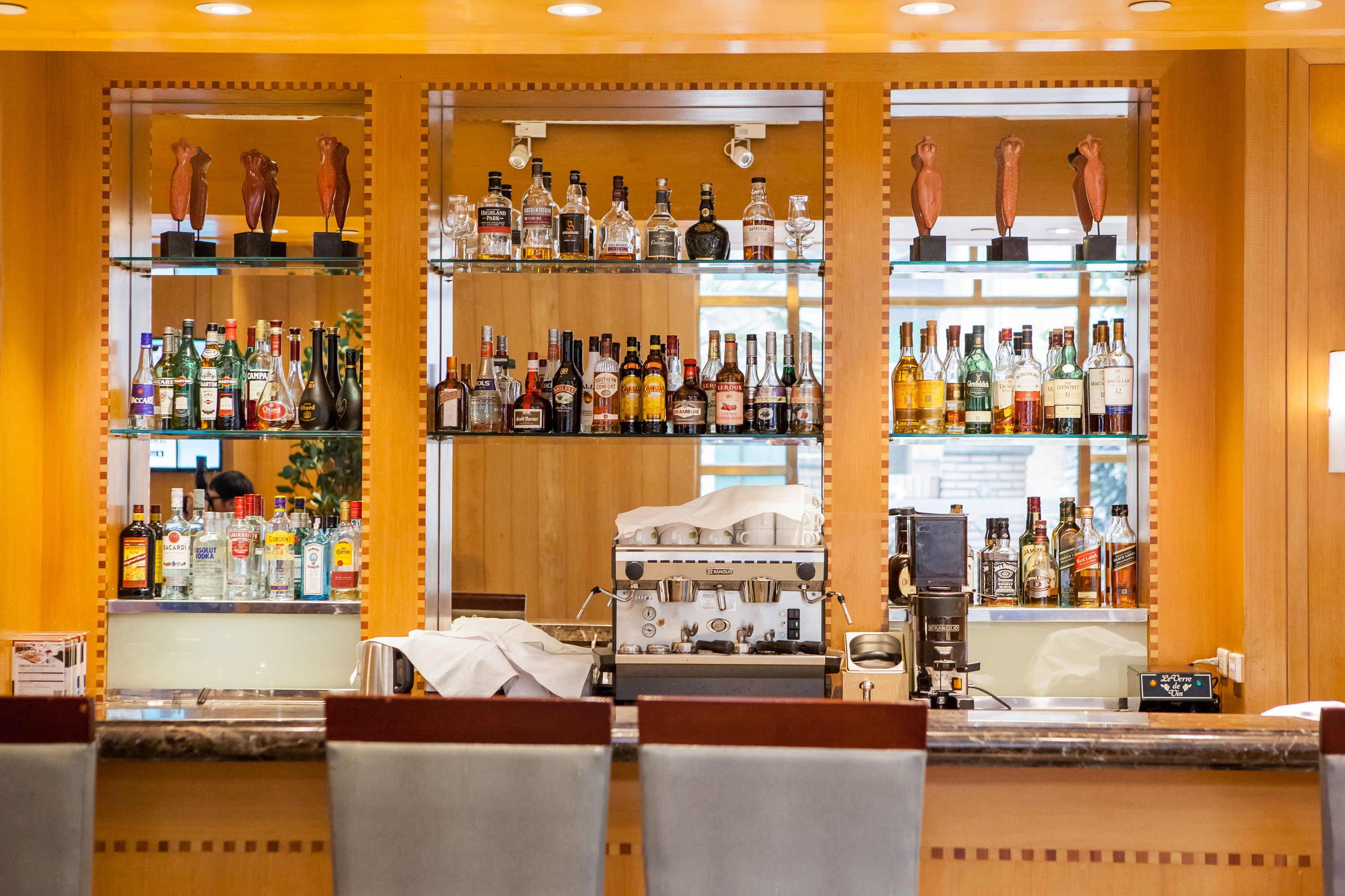 A bar area with multiple shelves of liquor bottles, a coffee machine, and seating.