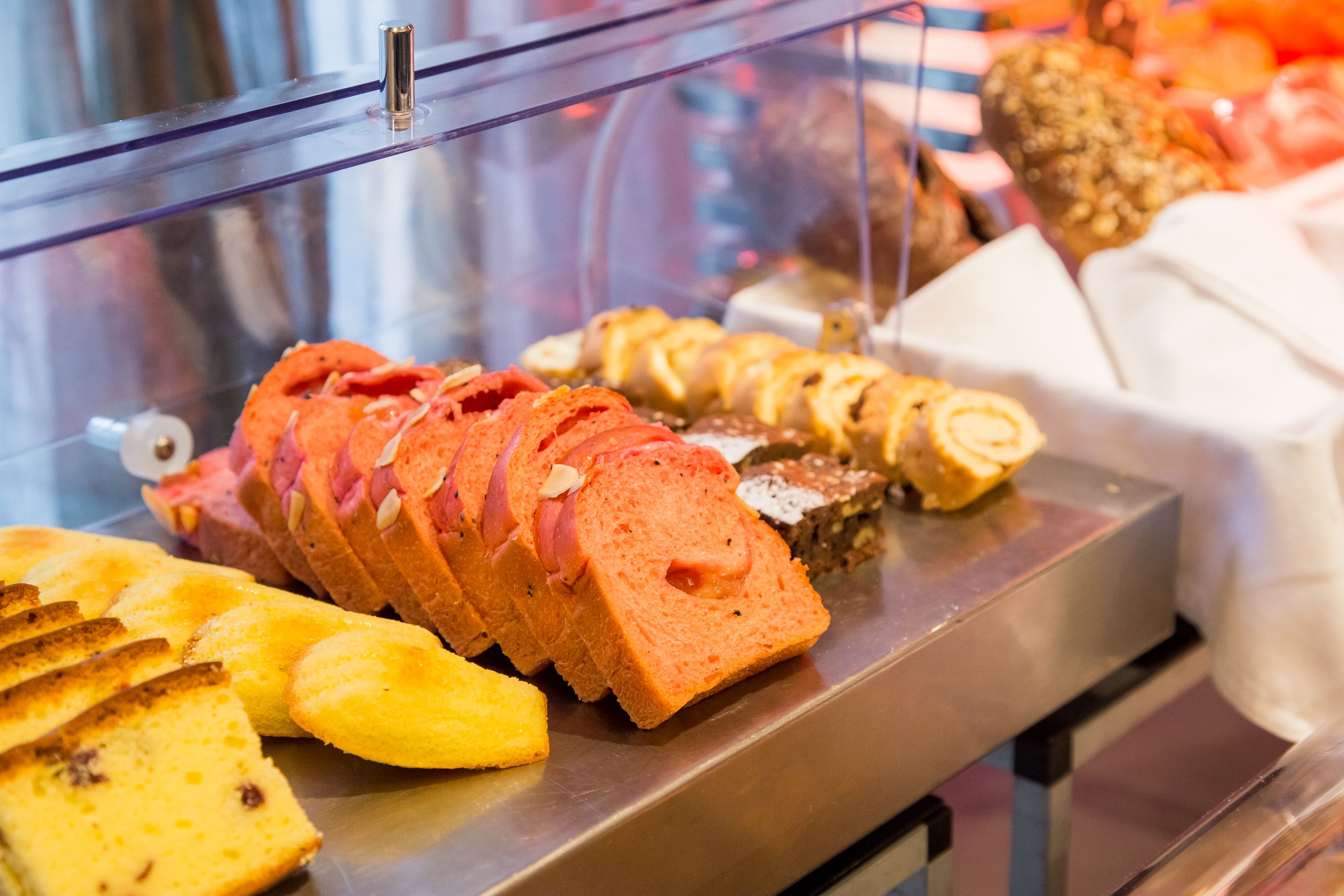A variety of baked goods displayed in a glass case, including bread, pastries, and rolls.