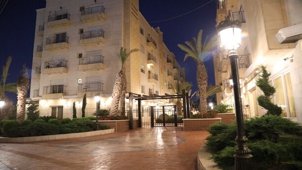 A multi-story hotel with a gated entrance, palm trees, and a well-lit pathway.