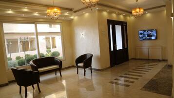 Eine Lobby mit einer Chandelüster, einem Fernseher und einer Sitzecke mit einer Bank und Sesseln.