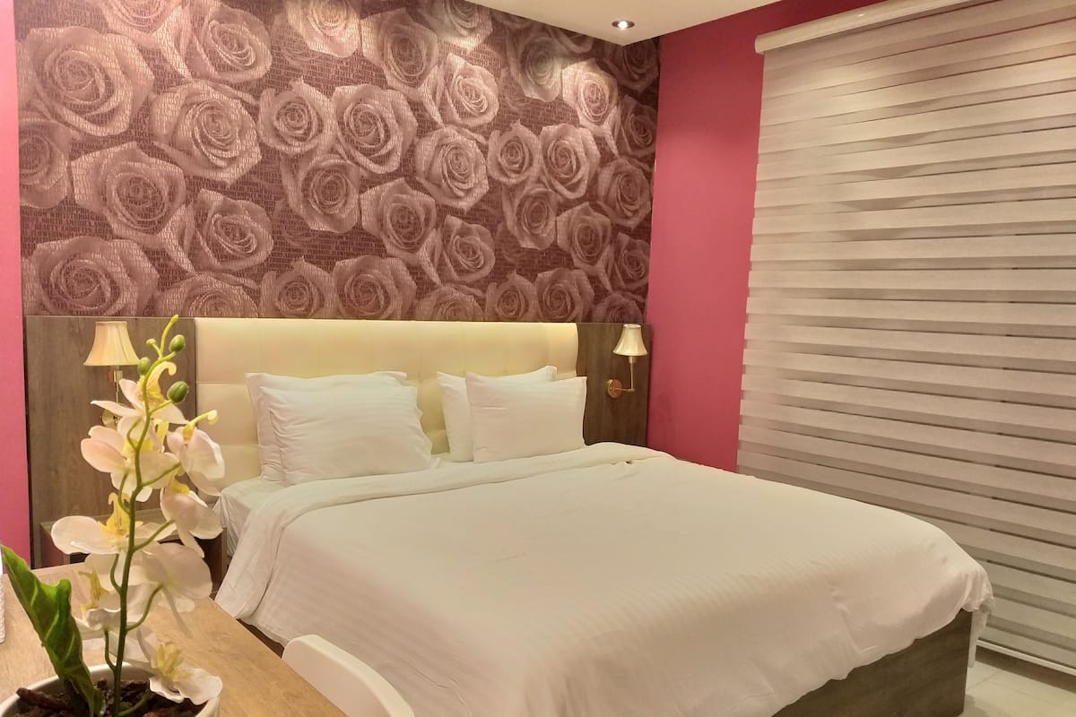 A bedroom with a bed, a nightstand, a potted orchid, and a wall with a floral pattern.