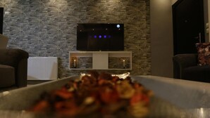 A living room with a stone wall, a flat-screen TV on a stand, a white console table, and a bowl of fruit on a table.