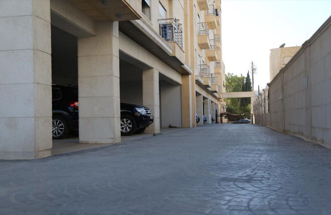 A narrow street with buildings on either side, featuring multiple parking spaces and balconies.