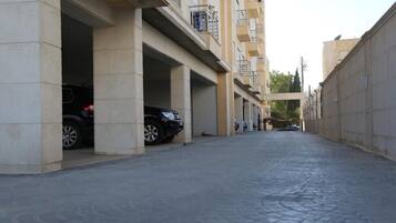 A narrow street with buildings on either side, featuring multiple parking spaces and balconies.